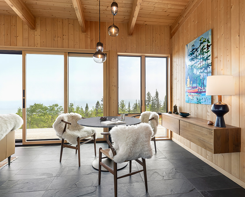 Cabin dining space with round table, wood chairs with sheepskin throws, and wall-mounted dining storage cabinet.